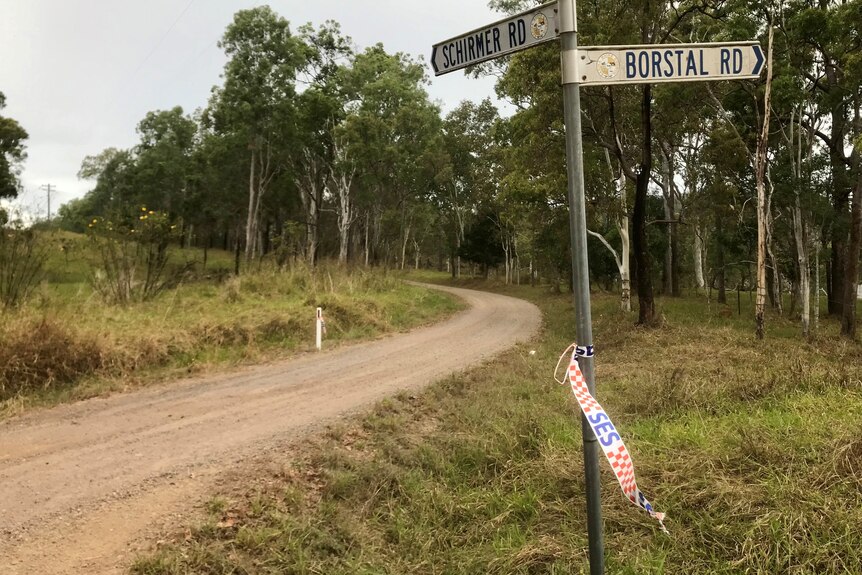 A dirt road with trees in the background. A street sign in the foreground has SES tape hanging off it. 