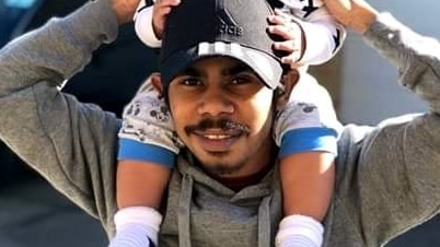 Man wearing a greay jumper and black cap, holding a young smiling child on his shoulders