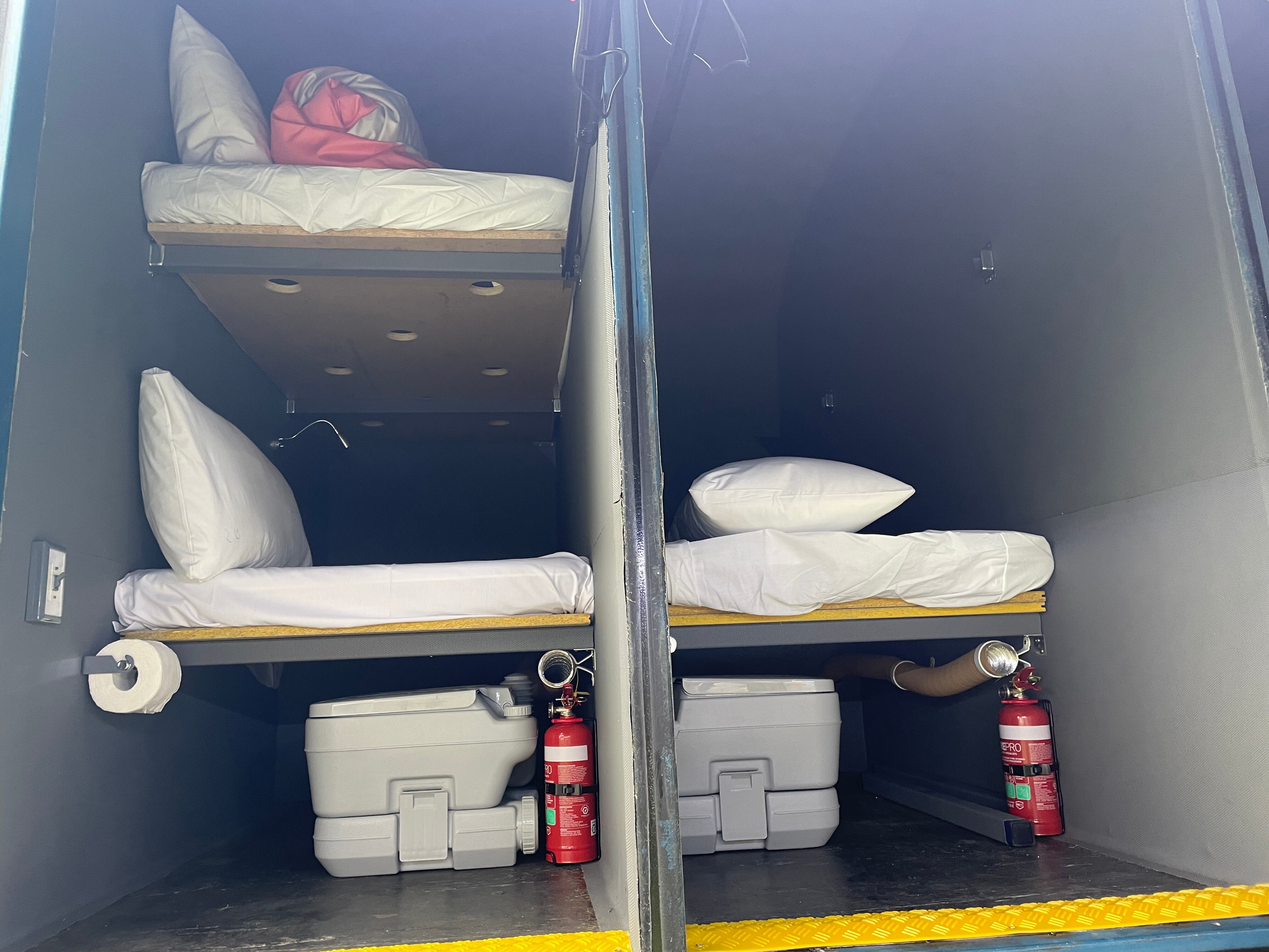 Two pods inside the sleep bus, the end of bunk beds visible and camp toilets underneath
