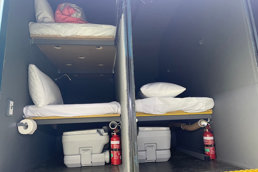 Two pods inside the sleep bus, the end of the bunk beds visible and the camp toilets below