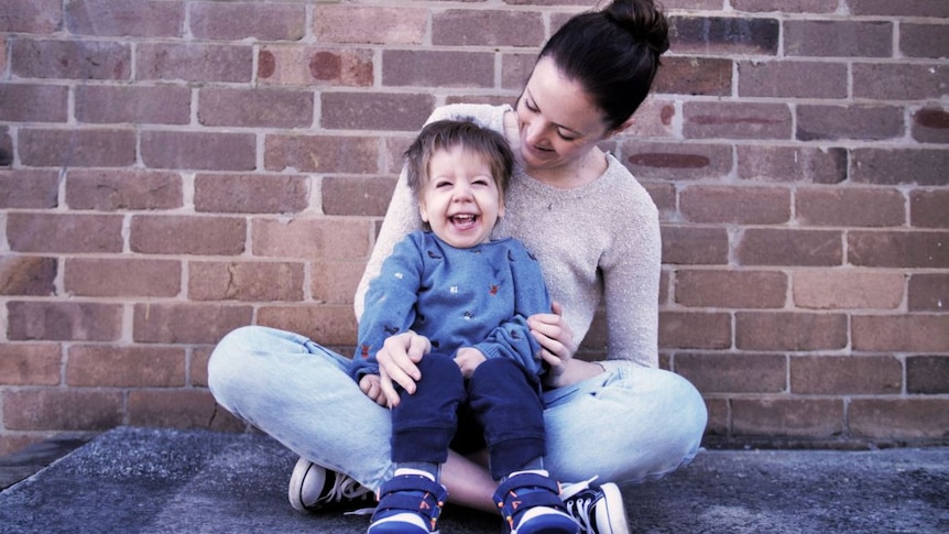 A mum sits on the ground with a small boy in her lap.