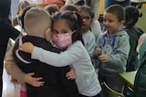 A girl in a mask hugs a boy in a black shirt.