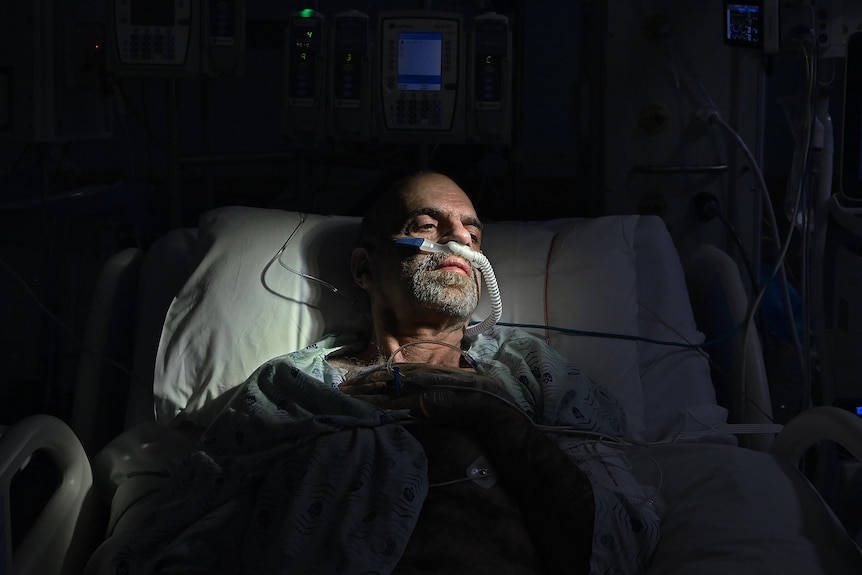 A man lying in bed, surrounded by tubes.