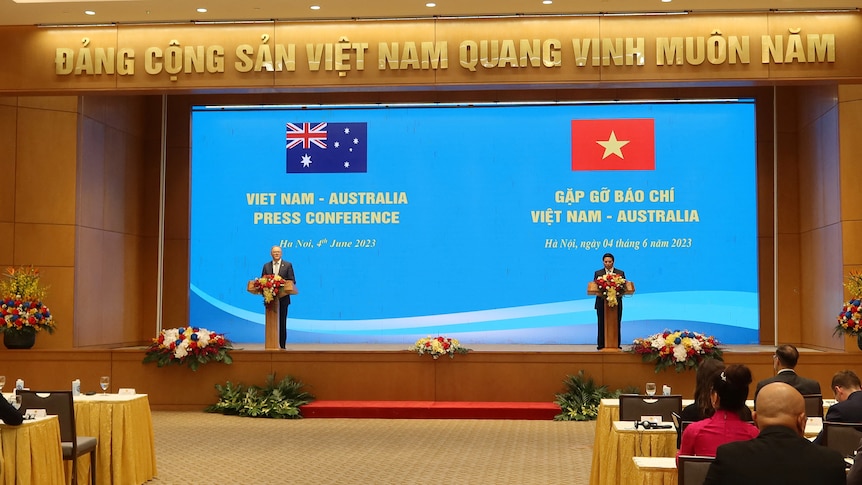 Two men stand on a blue-backgrounded stage with Australian and Vietnam flags behind