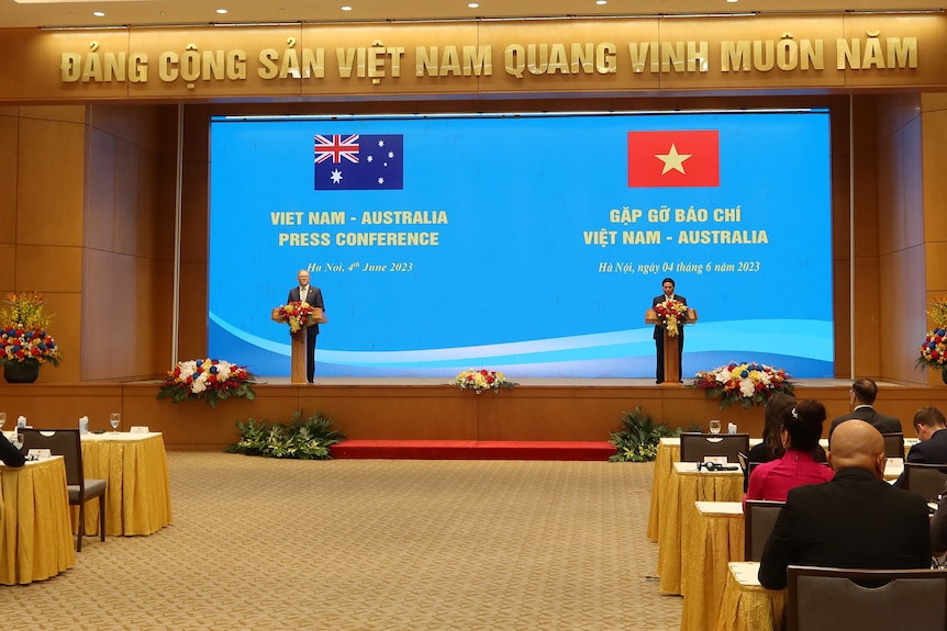 Two men stand on a blue-backgrounded stage with Australian and Vietnam flags behind