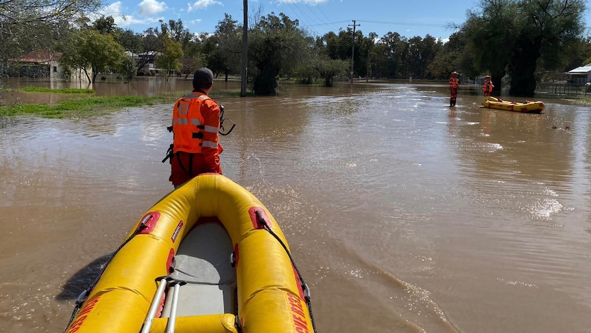 an emergency worker pulling a rubber dinghy over flood waters