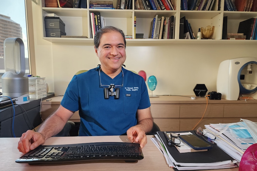 Dr Naveen Somia smiles sitting at his desk in his office.