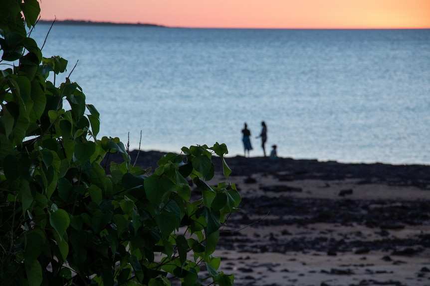 Two people stand at the beach and talk as the sun sets in Galiwin'ku.
