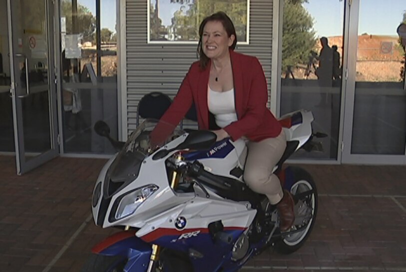 Labor's Darling Range by-election candidate Tania Lawrence sits on a white and blue motorcycle wearing a red jacket.