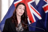 New Zealand Prime Minister Jacinda Ardern speaks in front of a New Zealand flag
