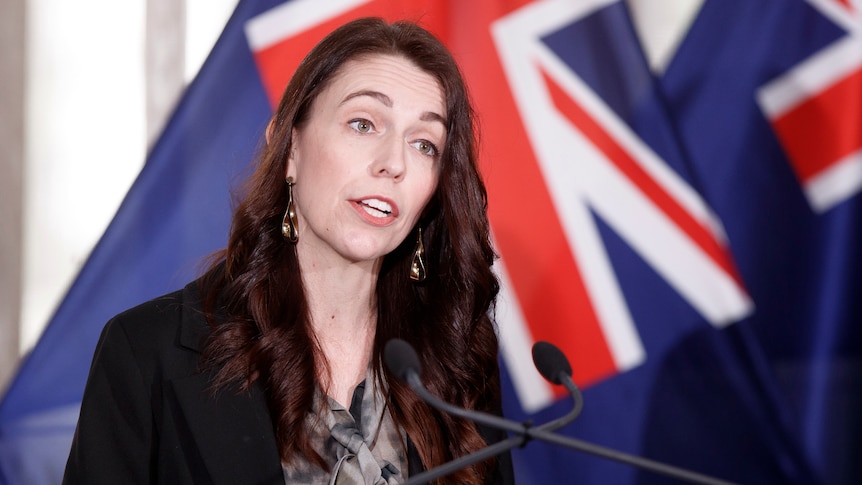 New Zealand Prime Minister Jacinda Ardern speaks in front of a New Zealand flag