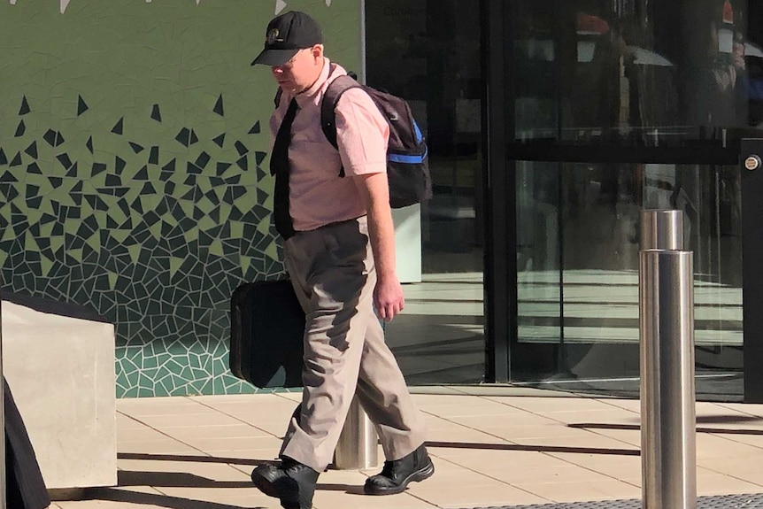 man in cap and pink shirt walking outside a court complex