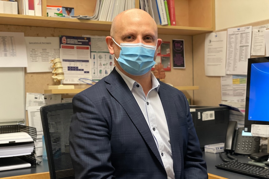 A man in a surgical mask sits in an office
