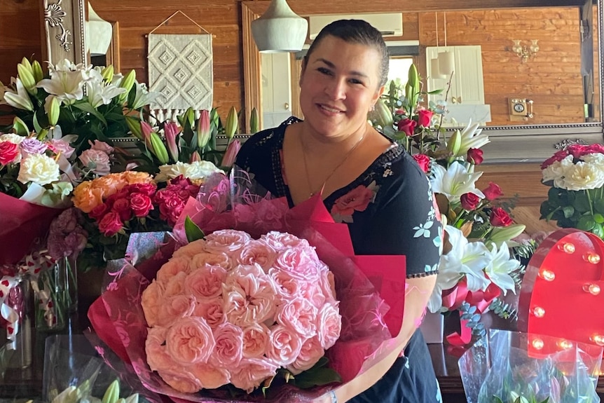 A smiling woman holds a large bouquet of flowers.
