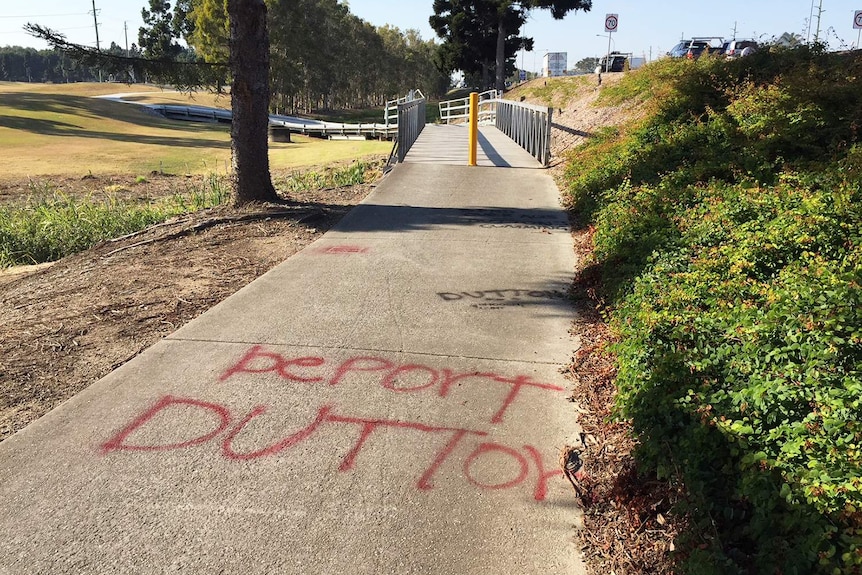 Graffiti 'Deport Dutton' spray painted in red on a footpath.