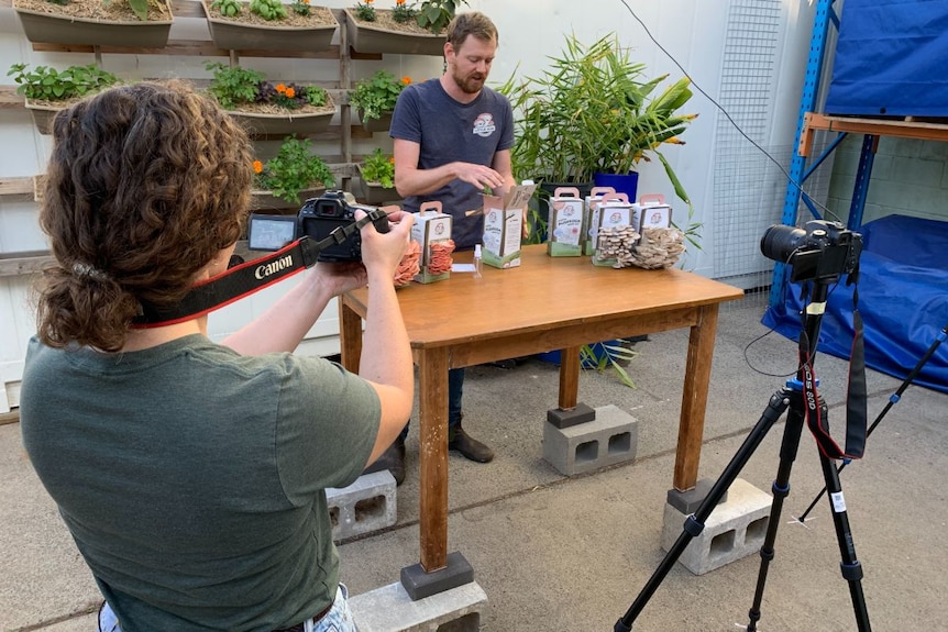 A woman with a camera films a man talking at a table.