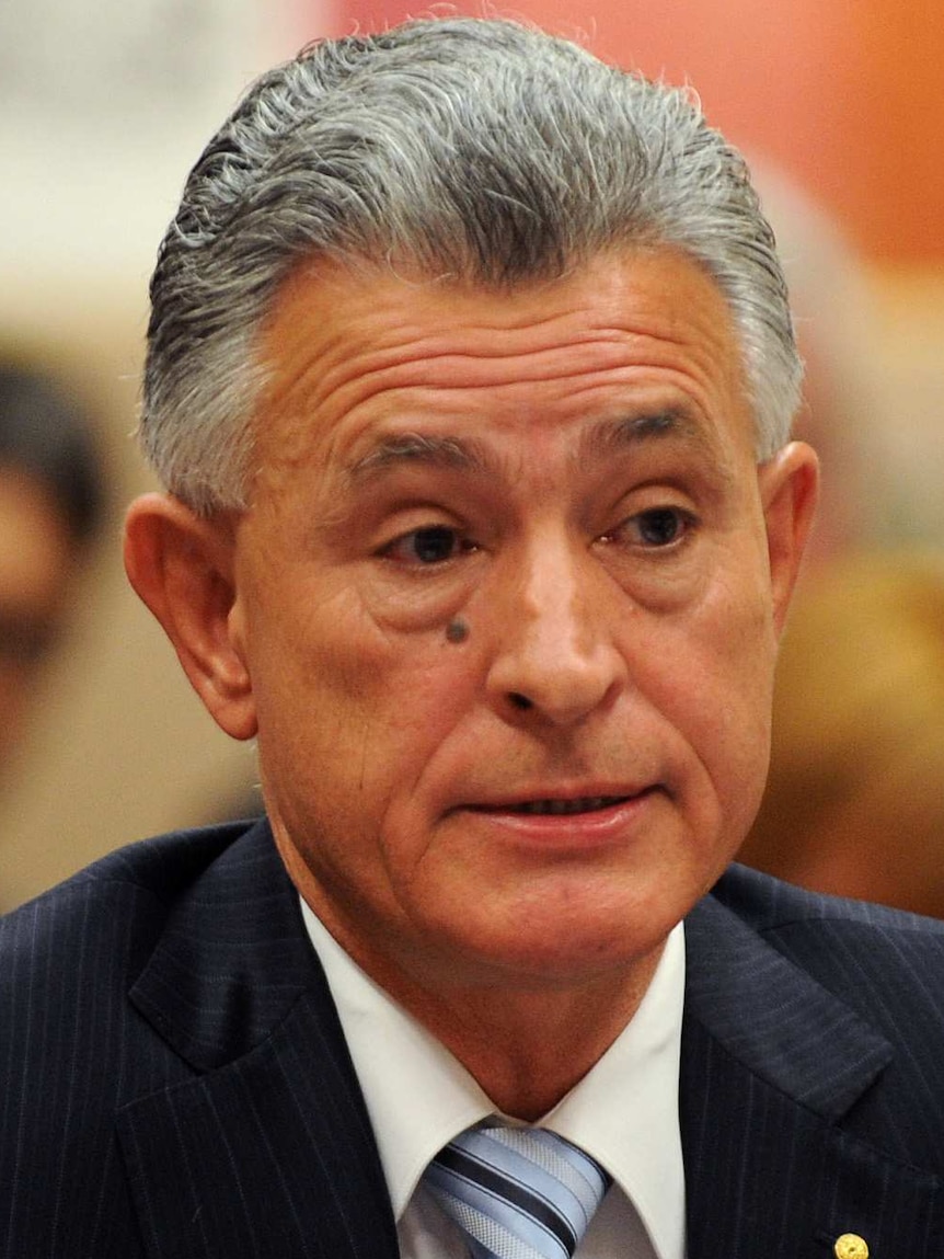 A man in a suit, sitting and speaking indoors