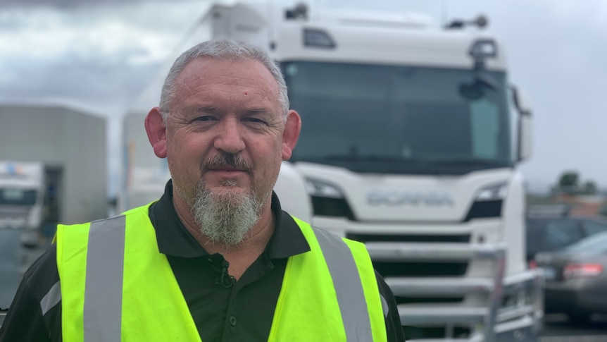 Man with beard in high vis vest stands in front of truck