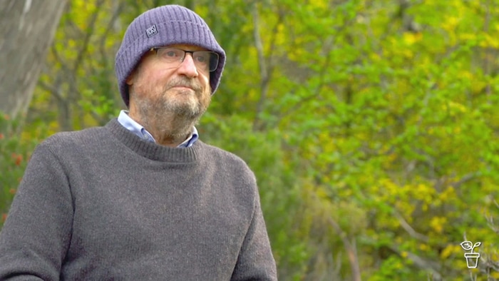 Man in a woollen jumper and beanie sitting out in the bush looking into the distance