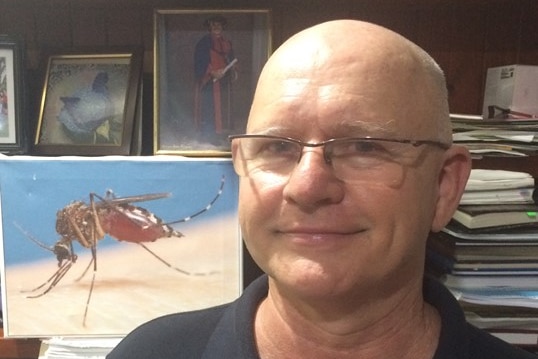 Man wearing glasses smiles in front of picture of mosquito