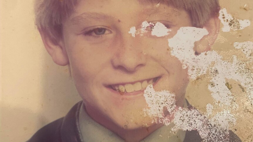 An old school photo of a young boy with blonde hair smiling.