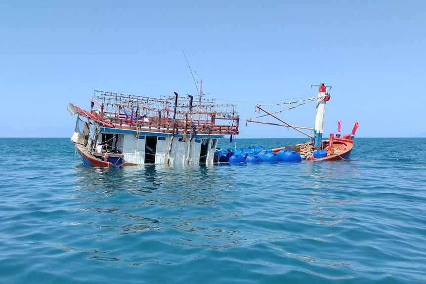 An old boat, viewed from the side, listing to one side, in the ocean on a sunny day with clear skies.