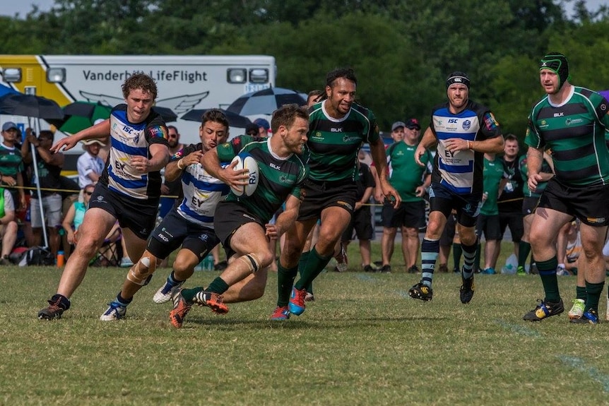 A Melbourne Chargers player runs with the rugby ball as another team tries to tackle him