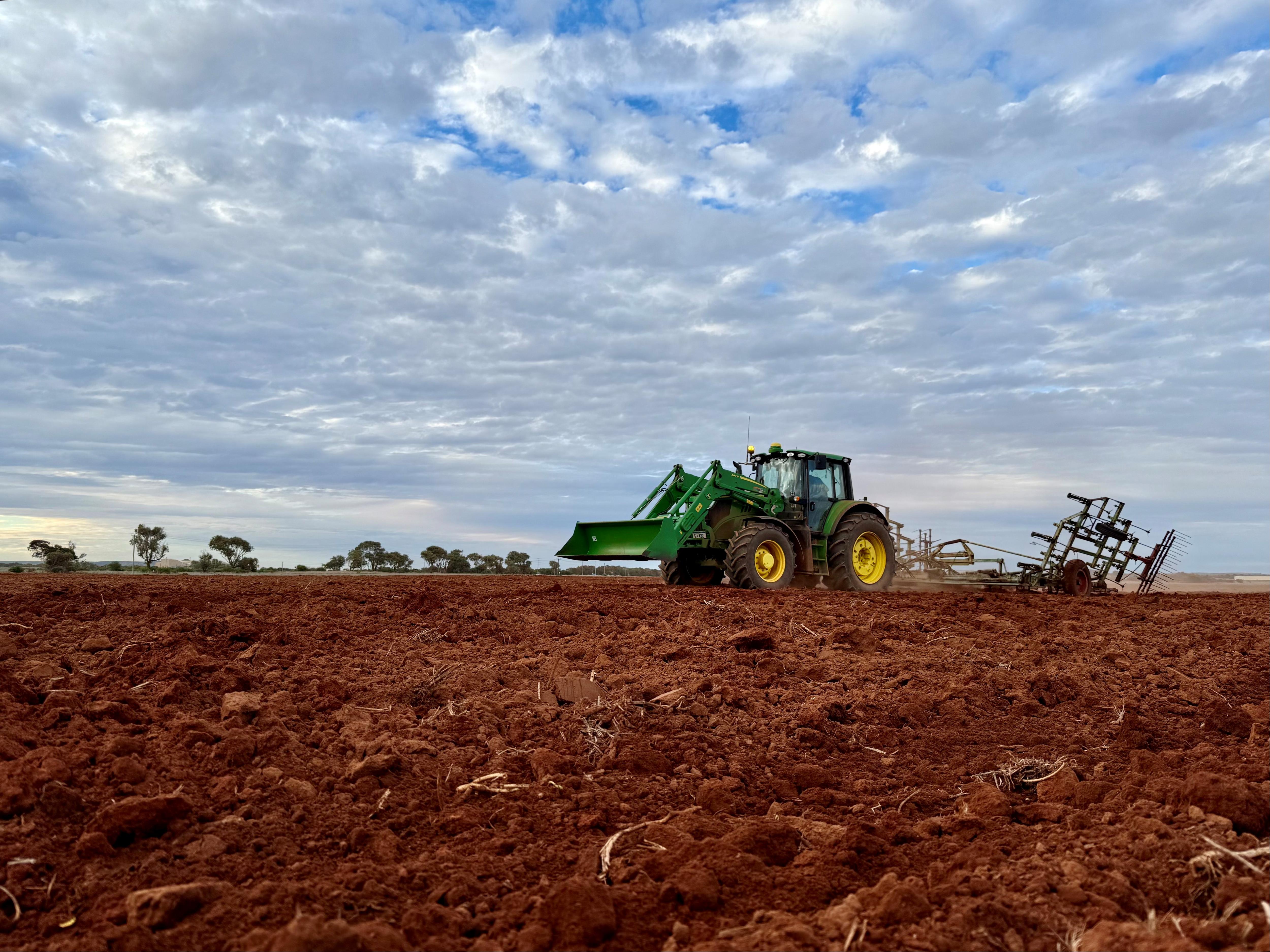 A tractor pulls a piece of machinery across red dirt.