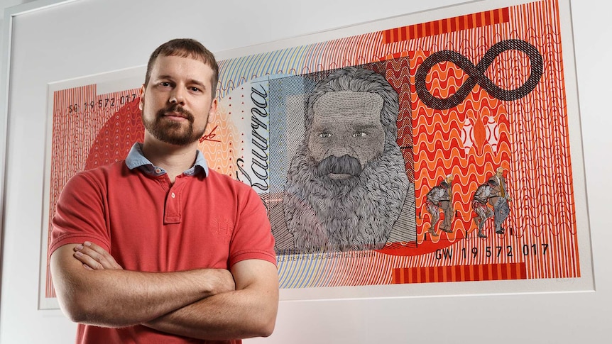 presley in a red shirt, arms crossed in front of his painting of the orange $20 note.