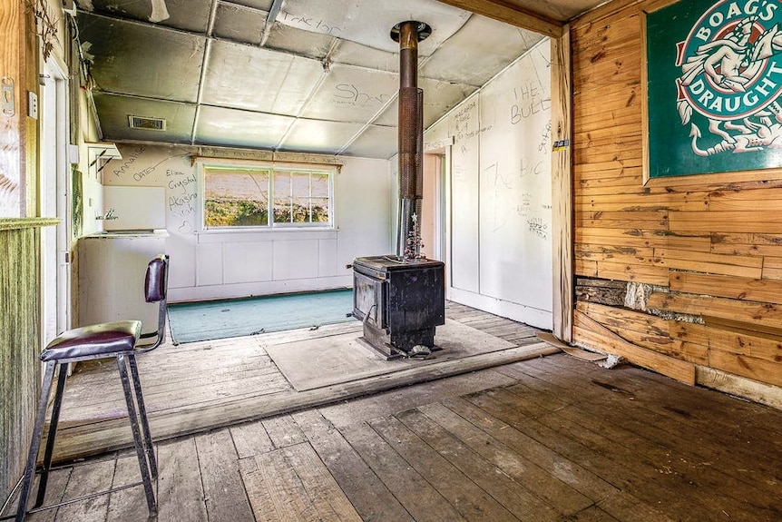 A rundown living room interior with wood-panelled walls and a wood-fired heater.