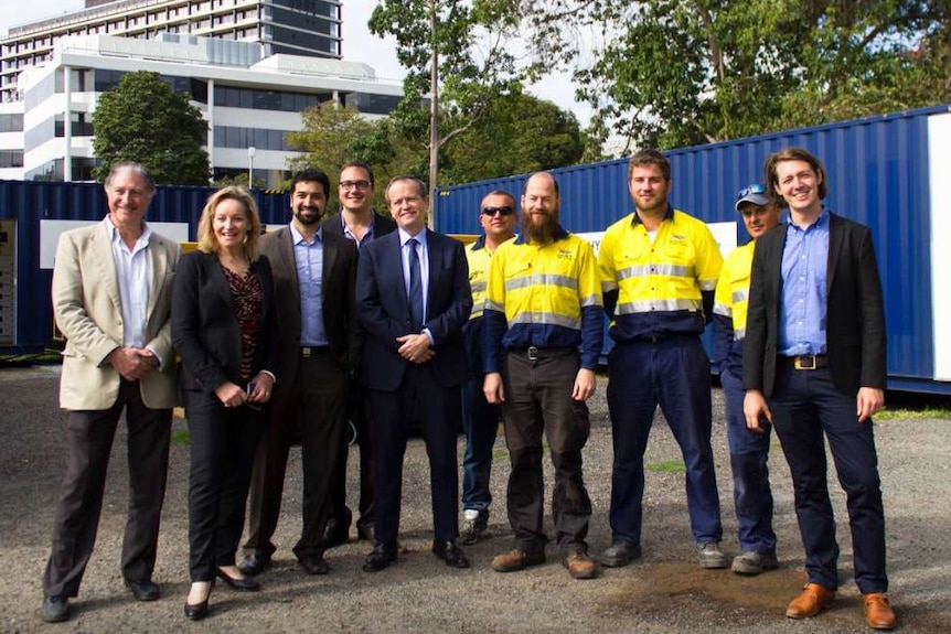 Alannah MacTiernan, Bill Shorten and people in suits and high-viz work gear pose at a work site.