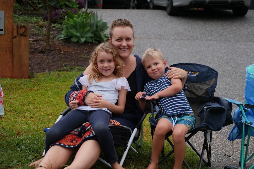A mother sits with her two kids on chairs on their driveway.