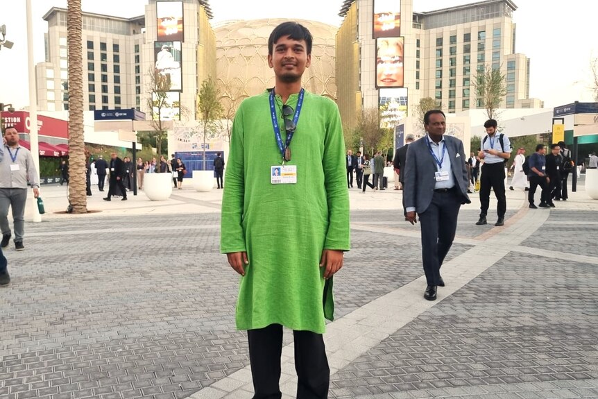 Indian man in long green shirt standing in the middle of a street in Dubai.