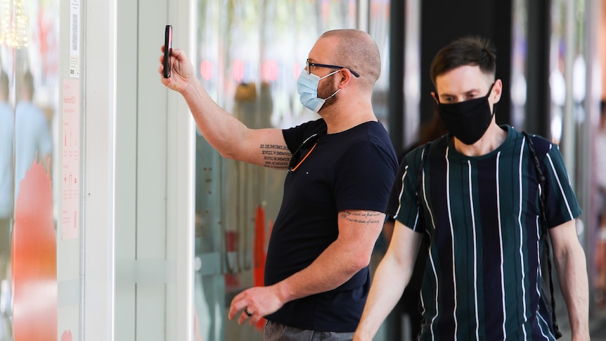 A man wearing a face mask uses his phone to scan into Safe WA.