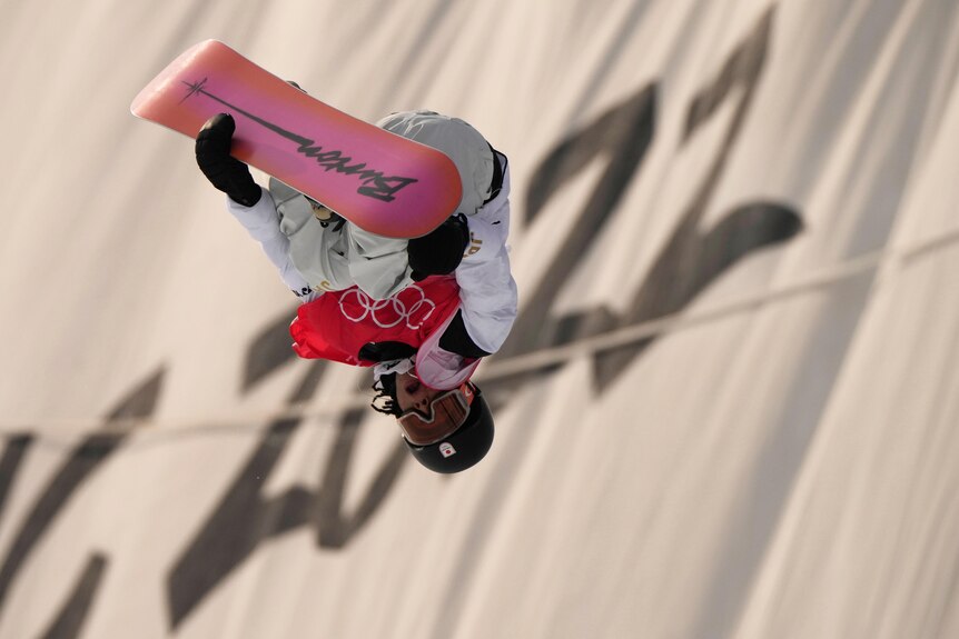 A snowboarder holds on to his board as he hangs upside down during a halfpipe run at the Winter Olympics.