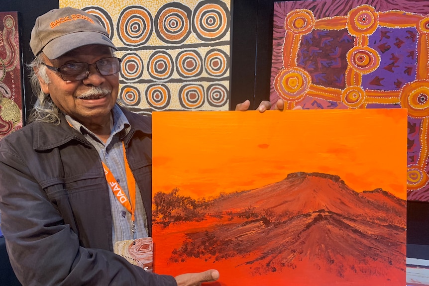 an aboriginal man wearing a cap carrying an orange painting