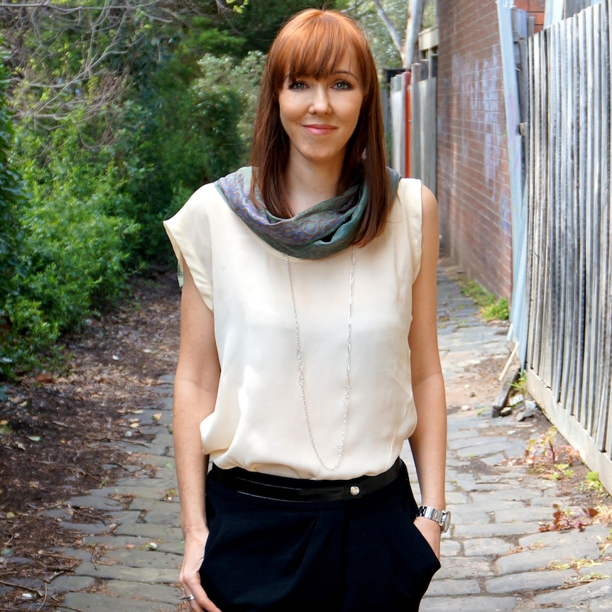 Rebekah has long red hair and stands in an alleyway.