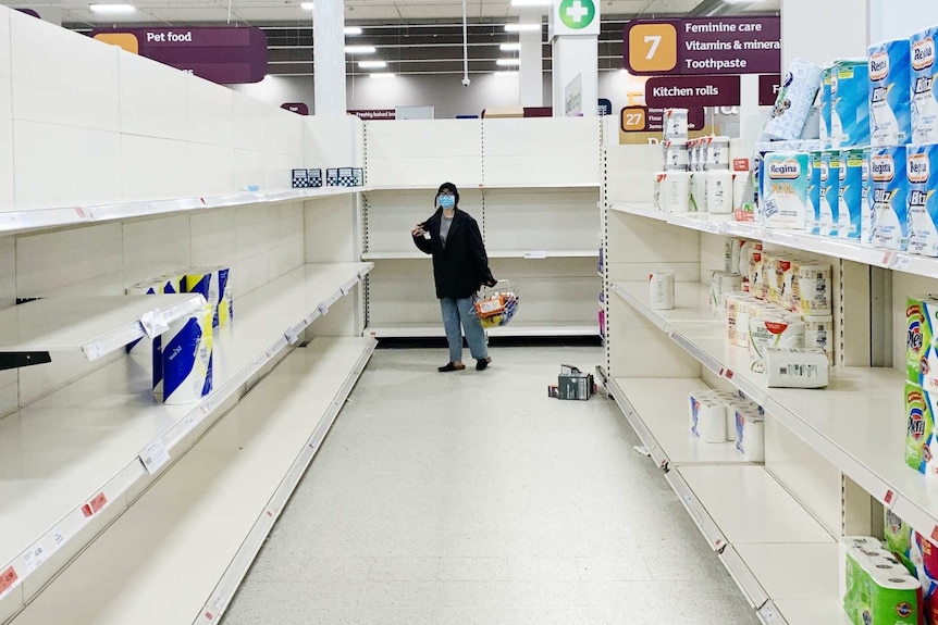 A woman wearing a mask in a nearly empty pharmacy aisle in a supermarket.