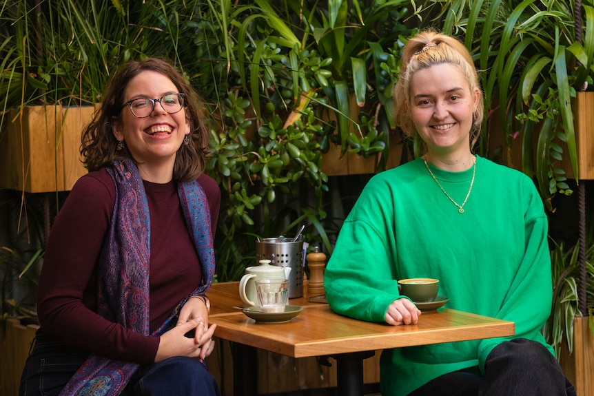 Megan Bennett and Anna Clark smiling while seated at a table having tea and coffee.
