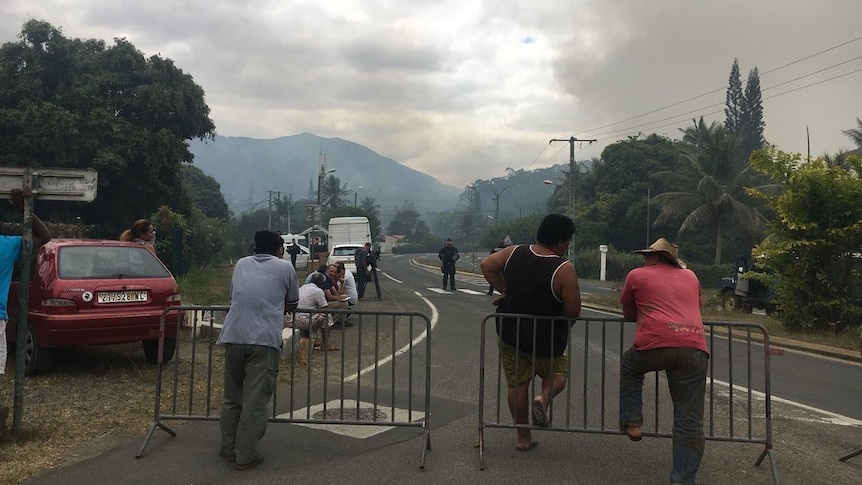 Residents watch smoke rising from behind a barricade.