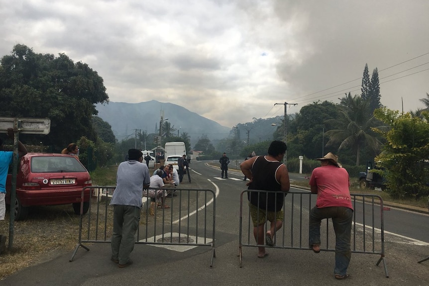 Residents watch smoke rising from behind a barricade.