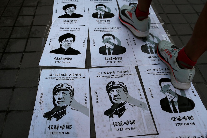 A closeup of a person stepping on posters of Mao Zedong, Carrie Lam and Xi Jinping. 