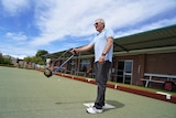 A man on a bowling green using an arm extension device to have a roll.