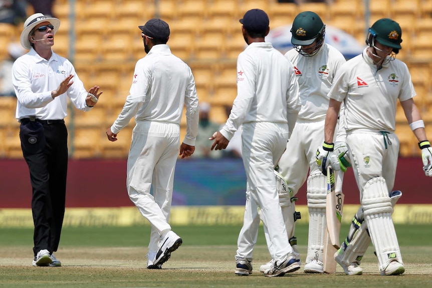 Virat Kohli speaks to umpire Nigel Llong as Steve Smith walks off the ground.