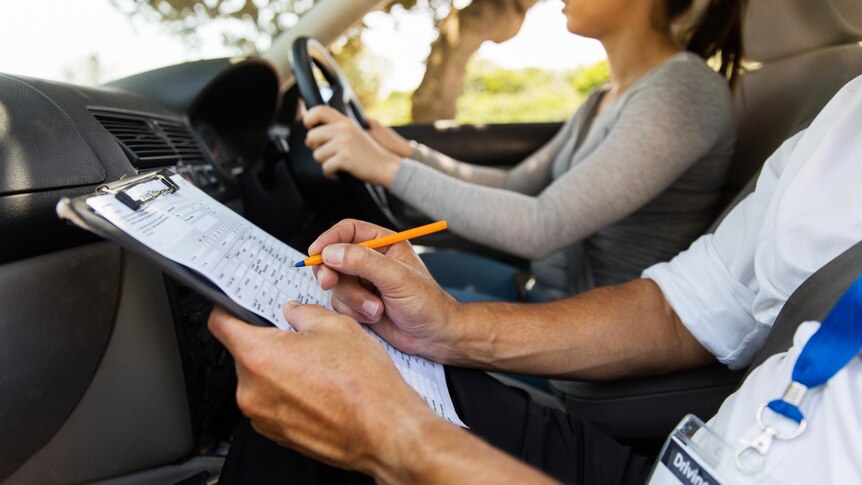 A male driving instructor sits beside a female student in a car