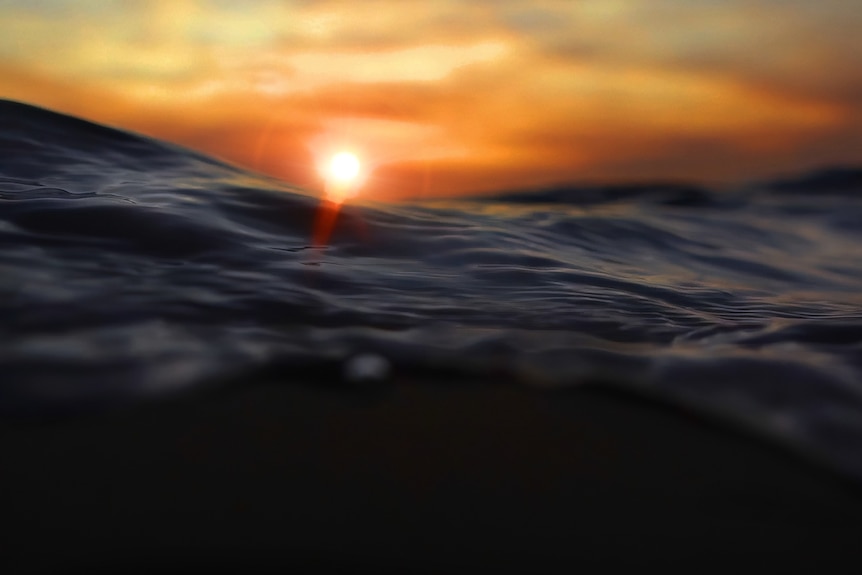 A photo of the ocean from in the water at sunset