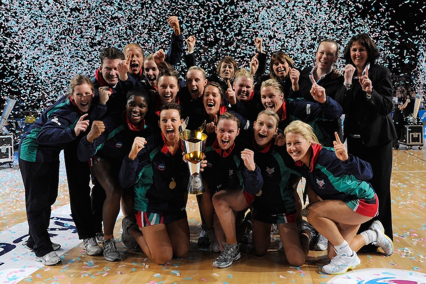 The Vixens team stand in a huddle and hold the trophy as confetti fires in the air