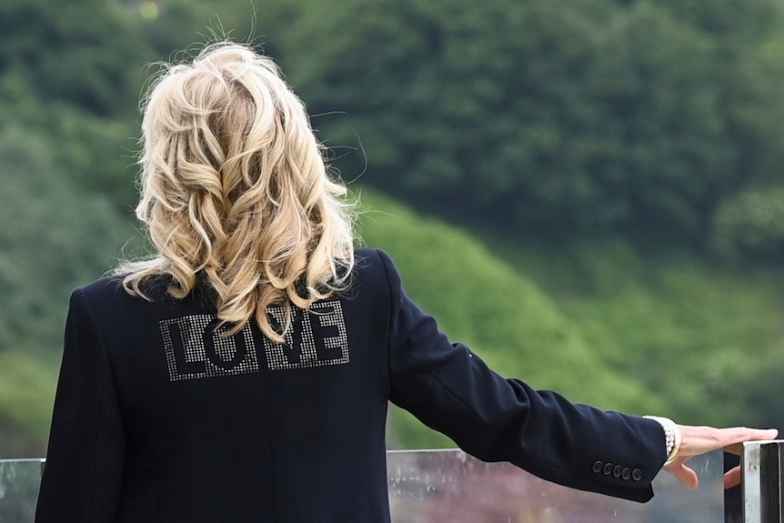 First Lady Jill Biden wears a black jacket with the word "Love" in bold letters printed across the back.