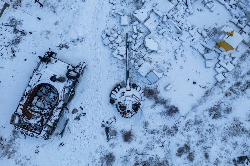 A destroyed tank in two large parts, covered in snow, stands in the yard of a house.