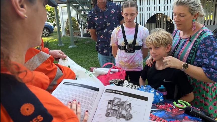 An SES worker with an emergency action guide, standing near a table with a young family